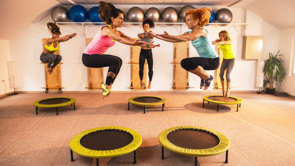Athletic women exercising in health club and jumping high up on mini trampolines.